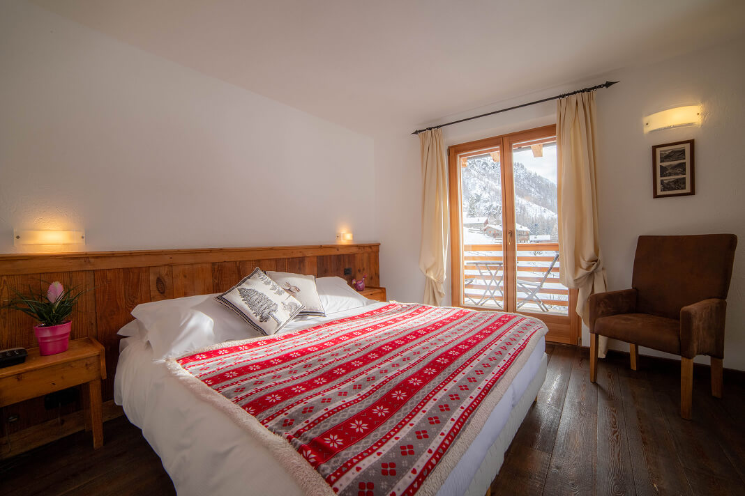 Camera Doppia Superior con letto matrimoniale, coperta alpina rossa, poltrona e balcone
