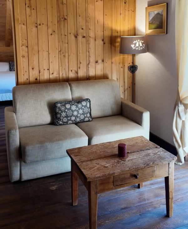 Angolo salotto di una camera con divano, tavolino in legno e parete rivestita in legno