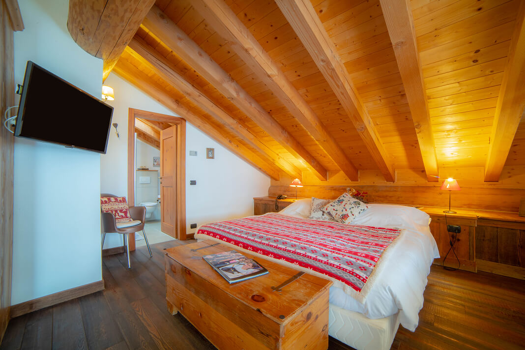 Camera Mansarda con soffitto a travi in legno e letto con coperta alpina rossa